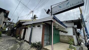 A hostel named Balai Vivencio Hostel with a signboard, a green door, and potted plants outside.