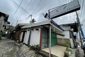 A hostel named Balai Vivencio Hostel with a signboard, a green door, and potted plants outside.
