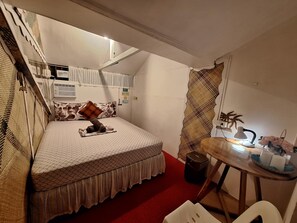 A compact room with a bed, a small table with a lamp, and a chair.