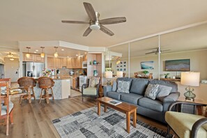 Ein geräumiger Wohnbereich mit grauem Sofa, Holzstühlen, einem Couchtisch und einem gemusterten Teppich.