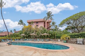 A swimming pool with lounge chairs and umbrellas, surrounded by palm trees and a building with balconies. - 1BD Near Kahana Beach Superb Ocean Views & Pool Sleeps 4 - Kahana Villa F410 (Lahaina)