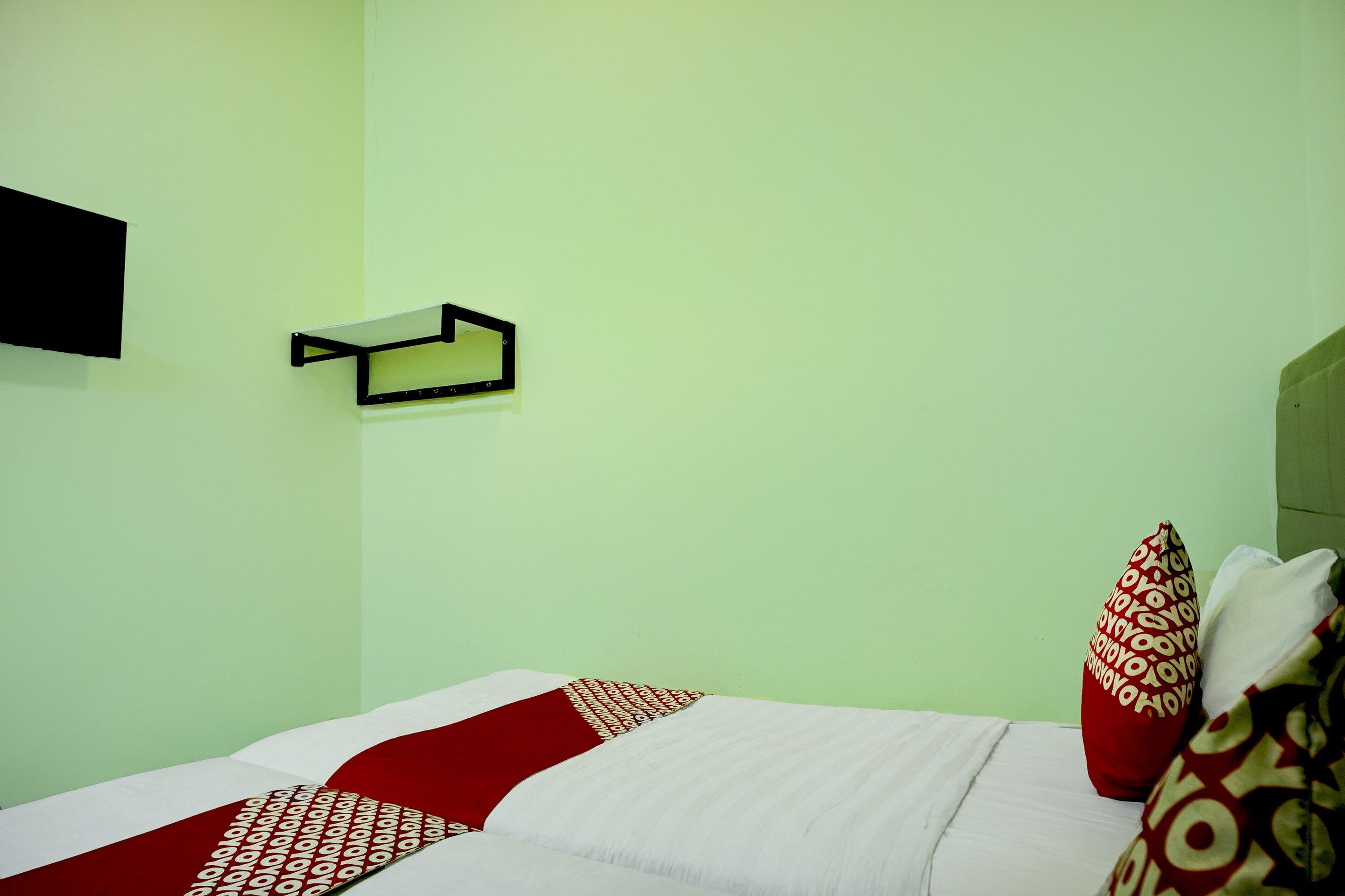A room with a bed, pillows, a wall-mounted shelf, and a wall clock.
