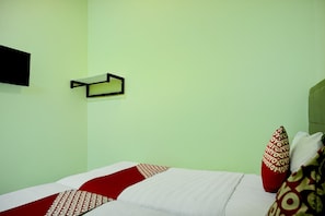 Quarto com cama, almofadas, prateleira na parede e relógio de parede.