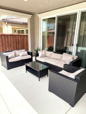 Eine Terrasse mit Korbmöbeln, darunter eine Sitzecke mit Sofa und zwei Sesseln sowie ein Couchtisch mit Glasplatte.