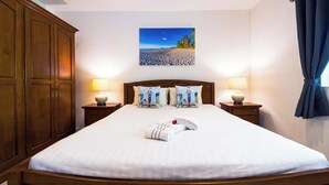 A hotel room with a large bed, two bedside tables with lamps, a wooden wardrobe, and a beach scene painting on the wall. - Cozy Luxury 2BR Pool Villa Retreat (PV1) (Hua Hin)