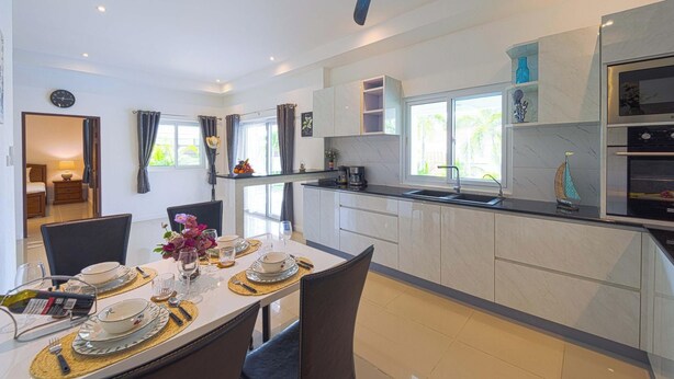 Cozinha moderna com ilha central, área de jantar com mesa posta para quatro pessoas e vista para o exterior através de grandes janelas.