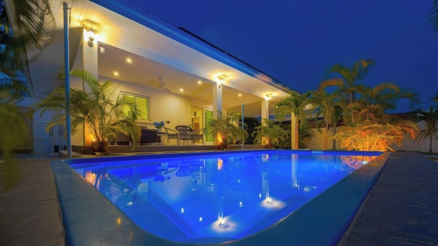 A swimming pool with a covered patio area, palm trees, and a building with outdoor seating. - Cozy Luxury 2BR Pool Villa Retreat (PV1) (Hua Hin)