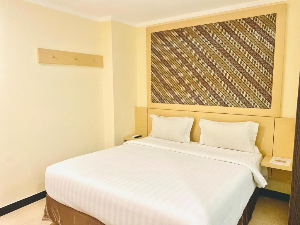 A hotel room with a bed, a headboard with a patterned design, a bedside table, and a nightstand.