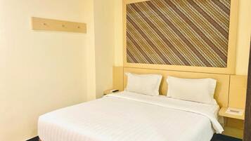 A hotel room with a bed, a headboard with a patterned design, a bedside table, and a nightstand.