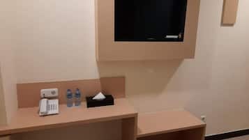 A hotel room with a desk, a telephone, two water bottles, a tissue box, and a television mounted on the wall.