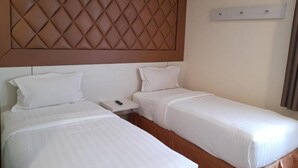 A hotel room with two beds, a headboard, a bedside table, and a wall-mounted light fixture. - Jakarta City Hotel (Kec.Taman Sari)