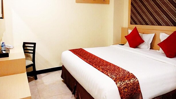 A hotel room with a bed, a desk, a chair, and a wall-mounted shelf. - Jakarta City Hotel (Kec.Taman Sari)