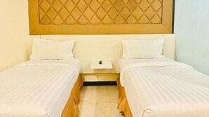 A hotel room with two single beds, a nightstand, and a headboard with a diamond pattern. - Jakarta City Hotel (Kec.Taman Sari)