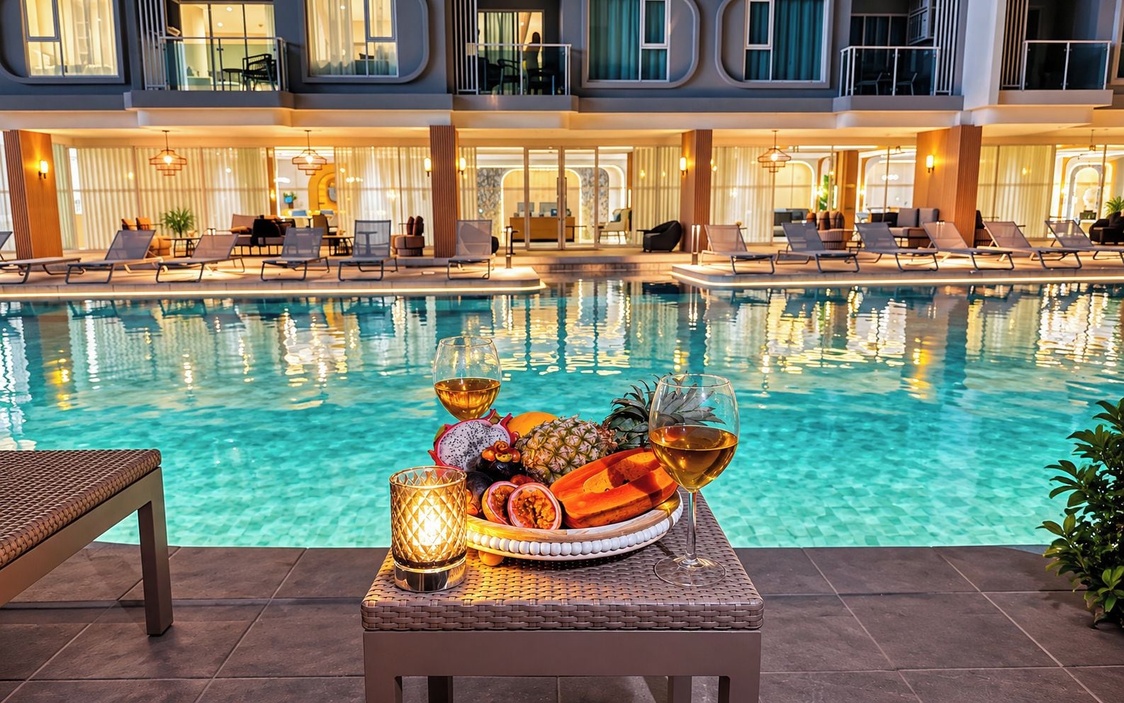 A poolside area with lounge chairs and a table with fruit and drinks.