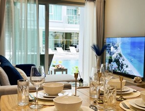 A dining area with a view of a pool and a balcony, a table set for a meal, and a television displaying a scenic view.