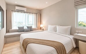 A modern bedroom with a large bed, a window seat with curtains, a bedside table with a lamp, and an air conditioning unit.