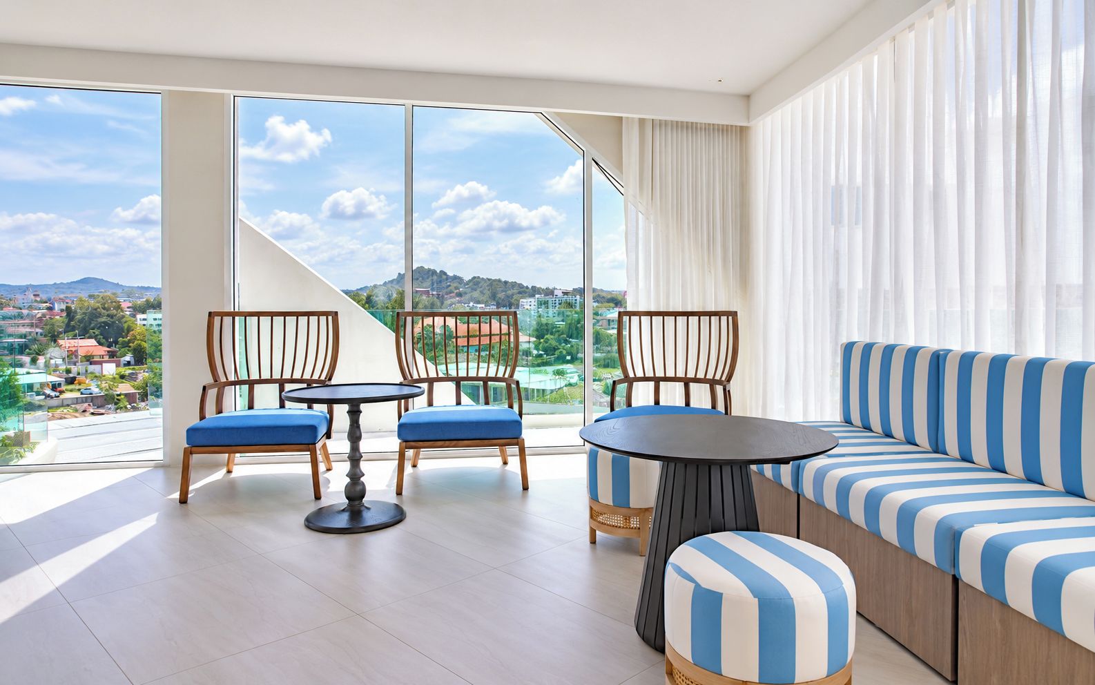 Uma sala de estar moderna com sofá, cadeiras, uma mesa redonda e amplas janelas com vista para a cidade.