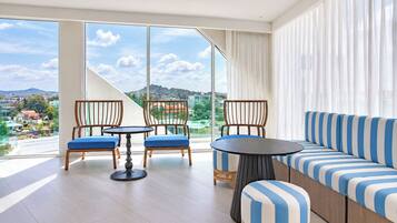 Uma sala de estar moderna com sofá, cadeiras, uma mesa redonda e amplas janelas com vista para a cidade.