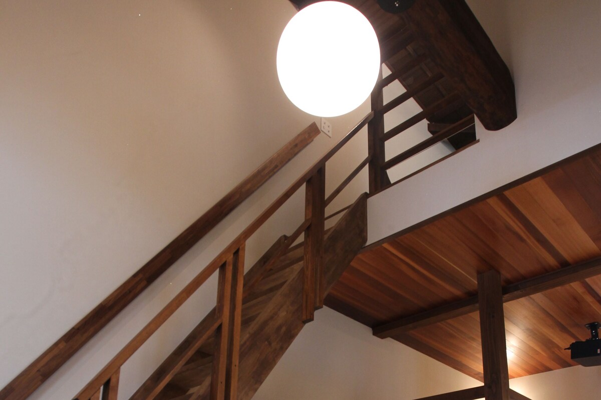 A loft-style room with a wooden staircase, a round table, and a built-in bench.