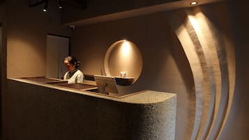 A reception desk with a person behind it, a round light fixture on the wall, and a textured wall design.