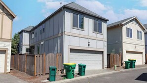 A two-story residential building with a garage, a wooden fence, and three green waste bins. - Comfortable Family Getaway ,Modern 3BR Home with AC & Quiet Neighborhood (Portland)