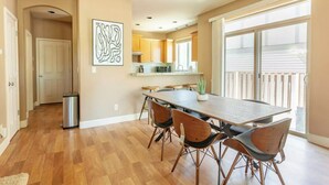 A dining area with a long table and chairs, a kitchen in the background, and a sliding glass door leading to a balcony. - Comfortable Family Getaway ,Modern 3BR Home with AC & Quiet Neighborhood (Portland)