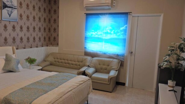 A bedroom with a bed, a sofa, a chair, a small table with a plant, and a window with a view. - Jomtien Beach Stay (Pattaya)