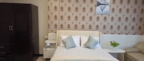 Una habitación de hotel con una cama, una mesita de noche, un armario y un sofá.