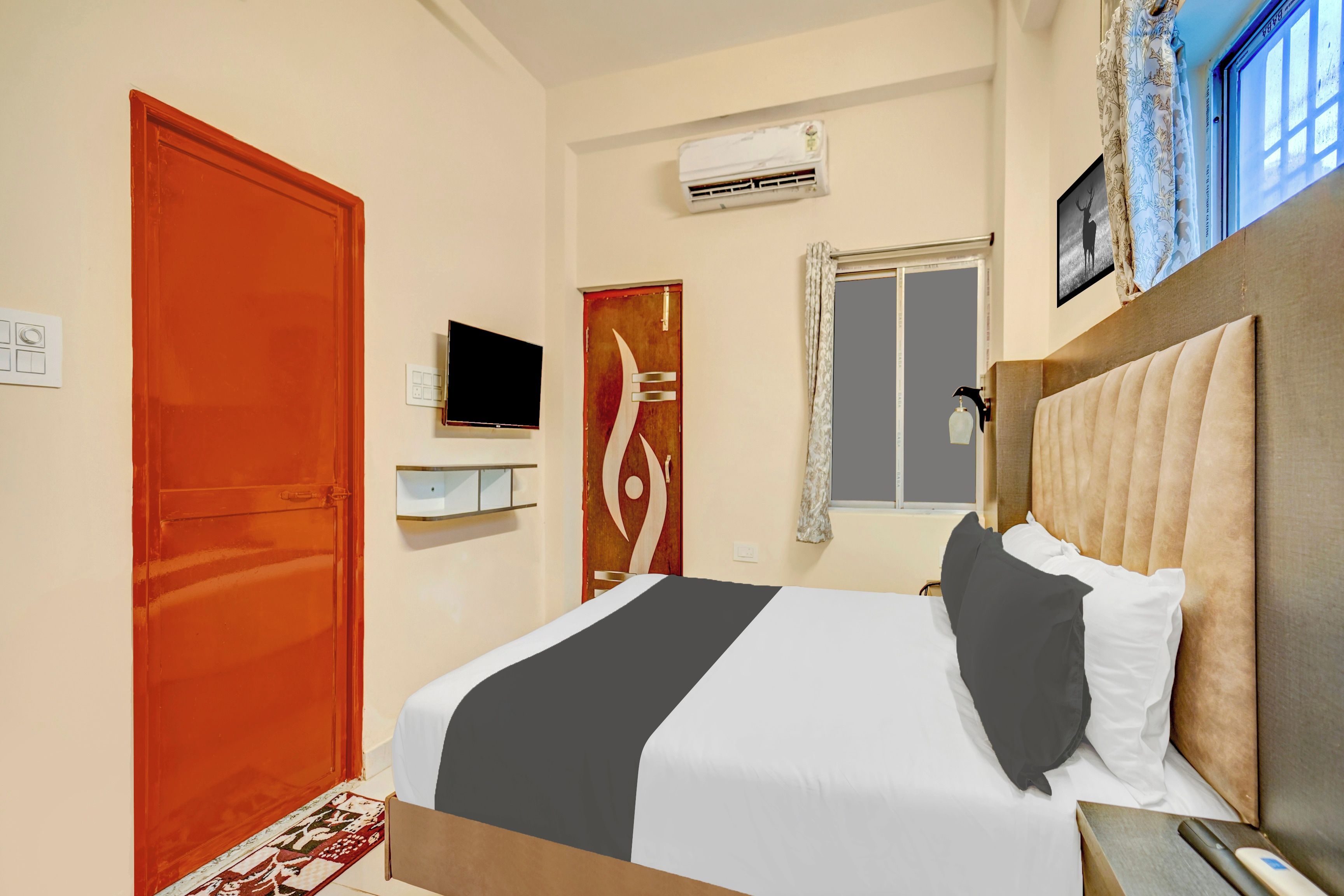A hotel room with a bed, a television, an air conditioning unit, a window with curtains, and a door.
