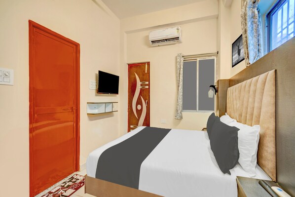 A hotel room with a bed, a television, an air conditioning unit, a window with curtains, and a door.