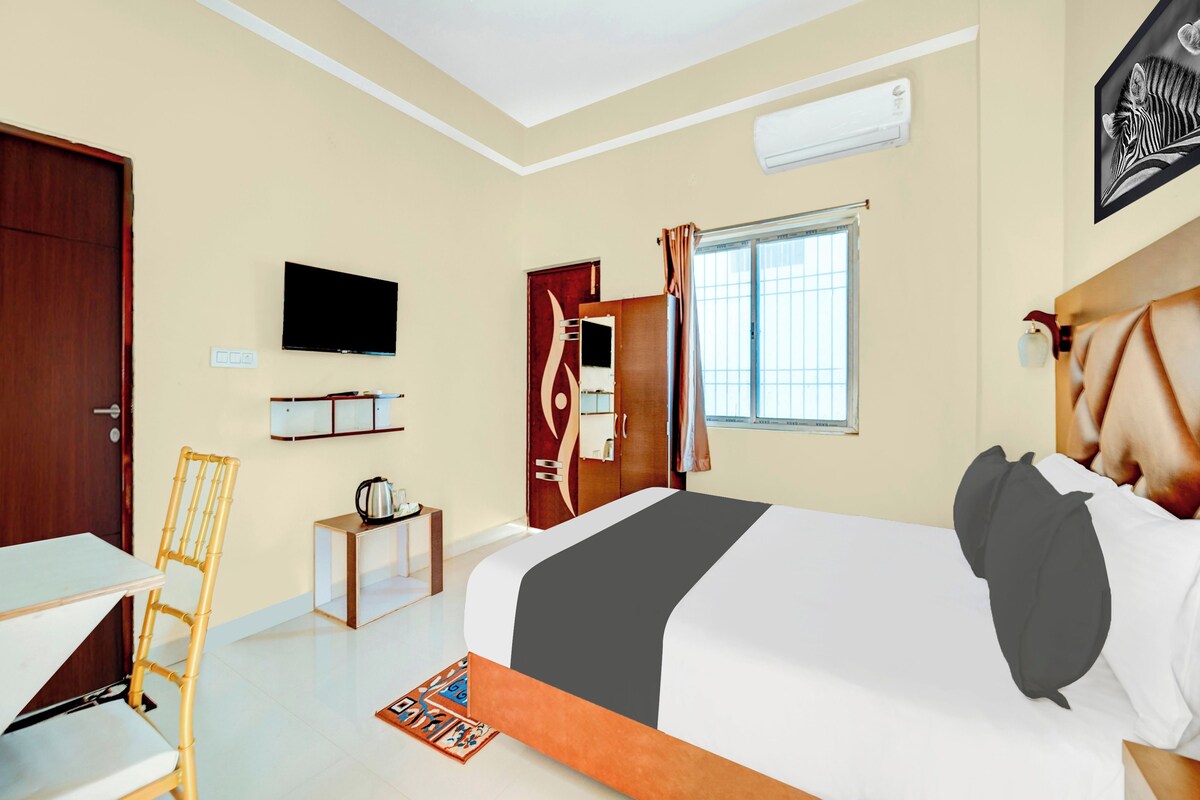 A hotel room with a bed, a television, a desk, a chair, a window, and an air conditioning unit.