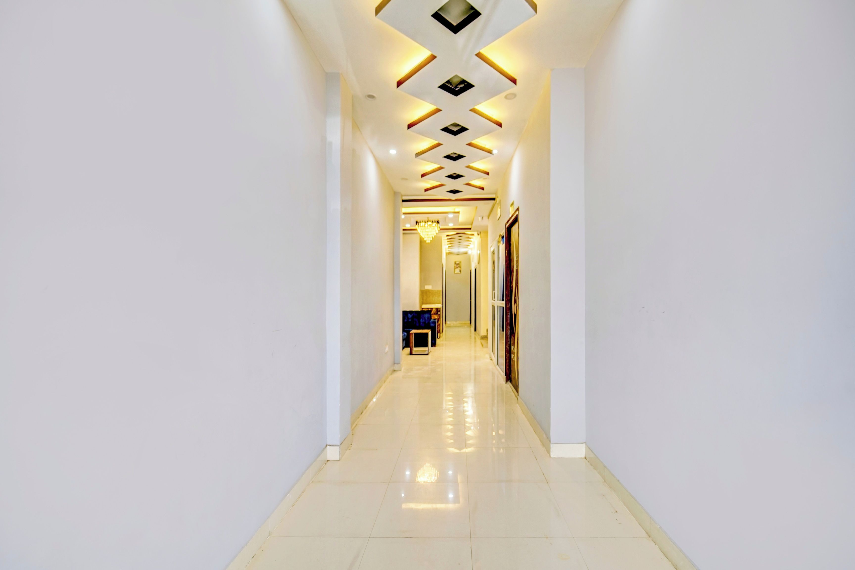 A long, narrow hallway with a reflective floor, leading to a room with a door at the end.