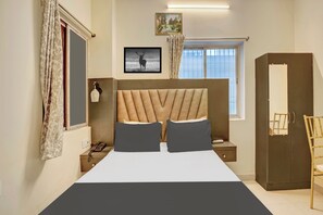A bedroom with a bed, a bedside table with a lamp, a wardrobe, and a window with curtains. - Super Townhouse Anisabad Near Mahavir (Patna)