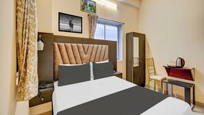 Habitación de hotel con una cama grande, una mesita de noche, una lámpara, un armario, una silla y una ventana con cortinas.