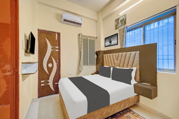 A hotel room with a large bed, a window with a view, a door with a unique design, and an air conditioning unit.