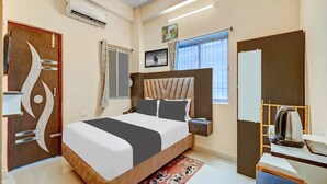 Habitación de hotel moderna con una cama grande, una mesita de noche, un armario, una ventana con cortinas, un equipo de aire acondicionado y un adorno en la pared.