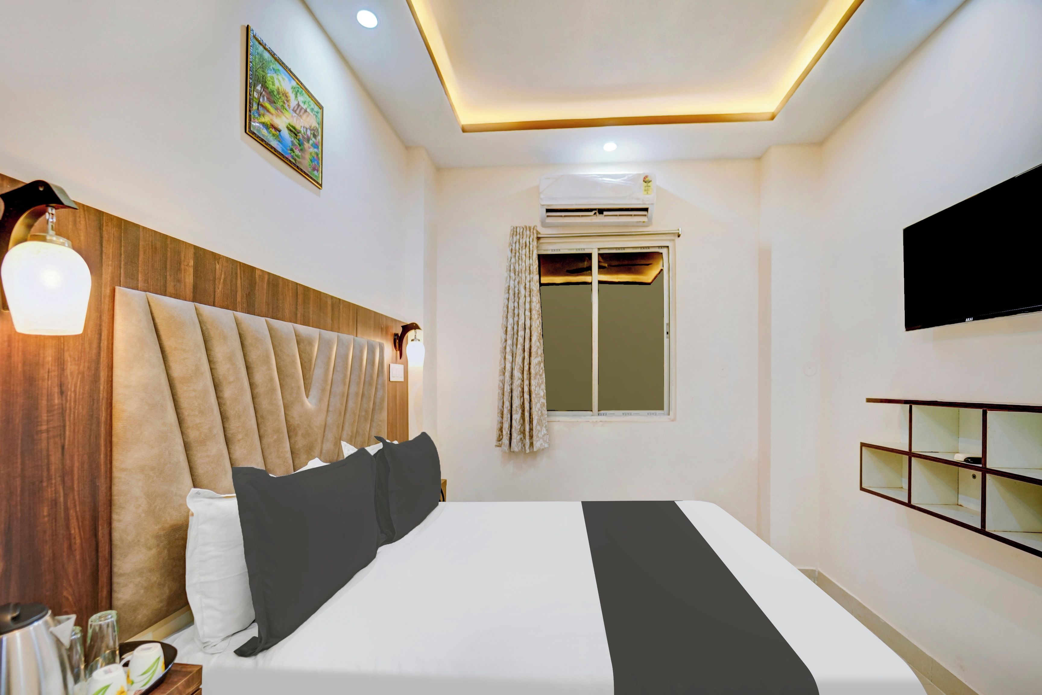 Habitación de hotel con una cama grande, un televisor de pantalla plana, una ventana con cortinas y un estante fijado a la pared.