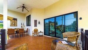 Une vaste terrasse dotée de meubles en osier, d’un ventilateur de plafond et d’une grande porte-fenêtre coulissante donnant sur l’extérieur.