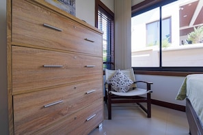 A bedroom with a wooden dresser, a chair with a patterned cushion, and a bed with a green blanket. - Stylish3BR PoolVilla,Prime Location-H146 (Hua Hin)