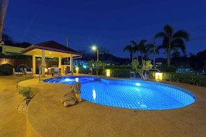 A swimming pool with a sunken center, surrounded by a covered seating area with chairs and a table, and a small building with a roof. - Stylish3BR PoolVilla,Prime Location-H146 (Hua Hin)