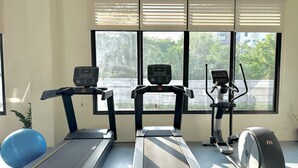 A gym with treadmills, an elliptical, and a stationary bike, with windows providing a view of greenery outside. - Royal Oceancrest Panglao 1 (Dauis)