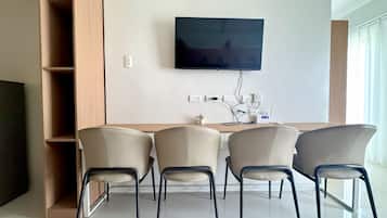 A modern living room with a flat-screen TV mounted on the wall, a wooden sideboard, and four chairs with metal legs.
