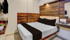 Ett hotellrum med en stor säng, en sänggavel i trä, en spegel, ett skrivbord med en telefon och en väggmonterad TV.