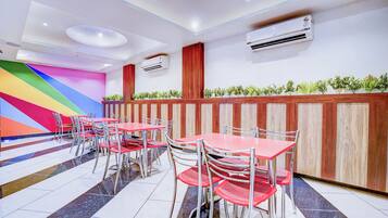 Interior de restaurante con mesas y sillas rojas, un muro colorido y un equipo de aire acondicionado.