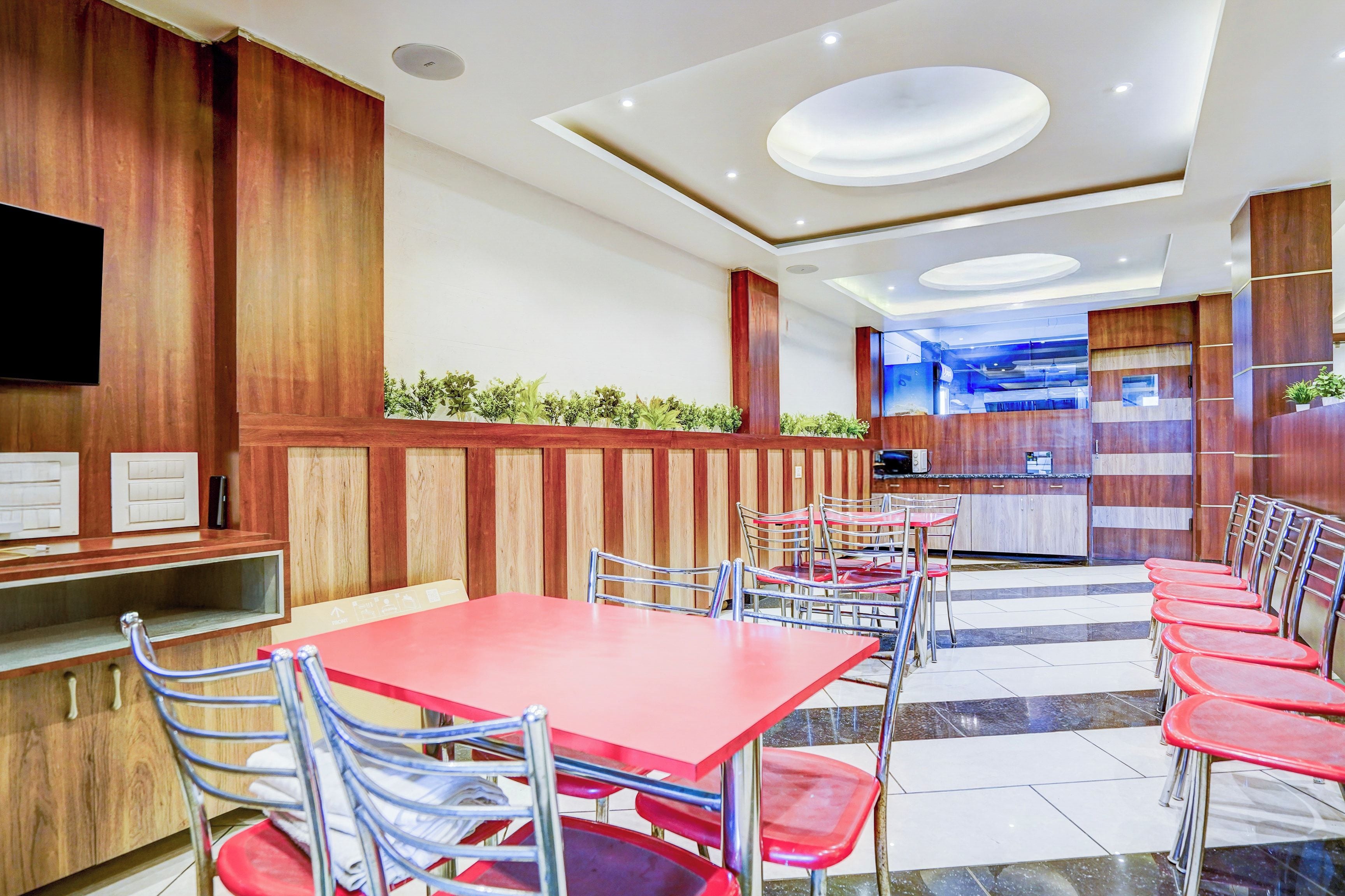Ein Restaurant mit roten Tischen und Stühlen, Holzwandverkleidung und einem Küchenbereich im Hintergrund.