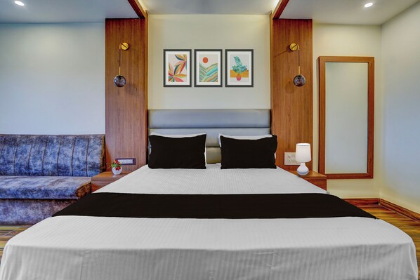 A hotel room with a large bed, a sofa, and three framed artworks on the wall.