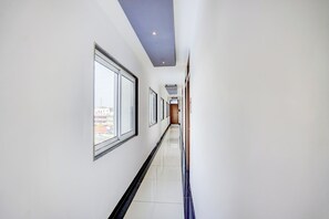 A corridor with large windows, a tiled floor, and a door at the end.