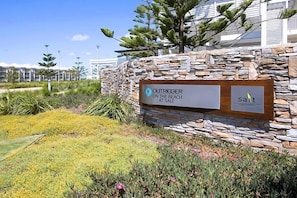A sign for 'Outrigger on the Beach at Salt' with a stone wall and landscaped garden. - The Pool Resort | Studio Pool View Getaway (Kingscliff)