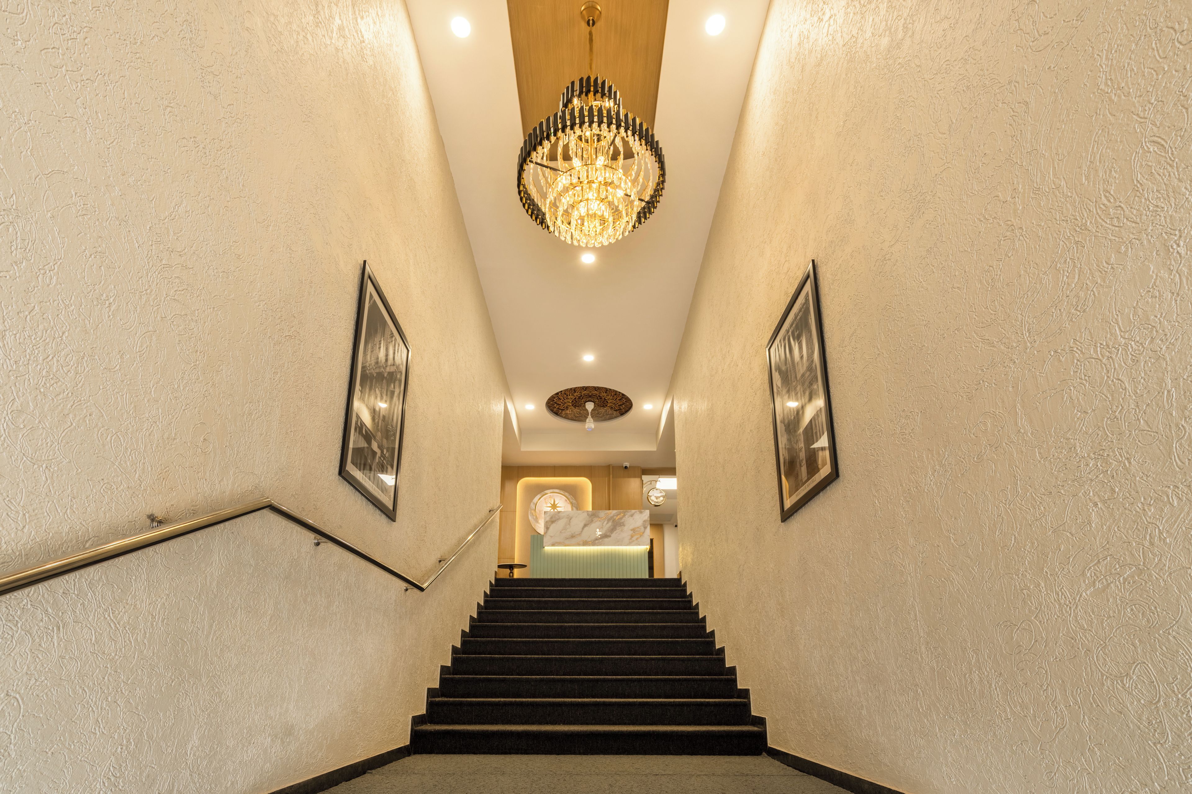 A grand staircase with a chandelier, framed pictures, and a reception area at the top.