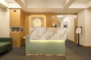 A reception desk with a marble top, wooden paneling, and a green upholstered chair. - The Estrela Hotel (Ahmedabad)